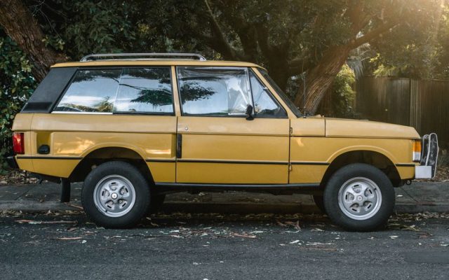 Side view of a classic yellow SUV parked on a tree-lined urban street during the day.
