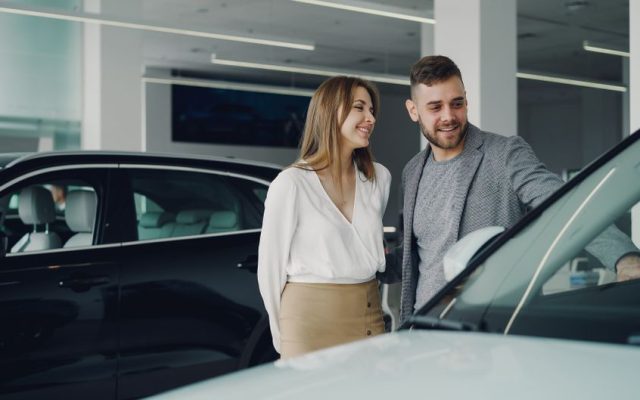 Smiling couple exploring cars at dealership, enjoying shopping experience.